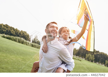 Weekend activities. Father carrying daughter on his back holding 44027042