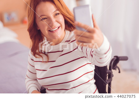 Joyful wheelchaired woman making selfies 44027075