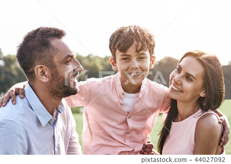 Bonding. Family of three walking on grassy field son hugging par 44027092