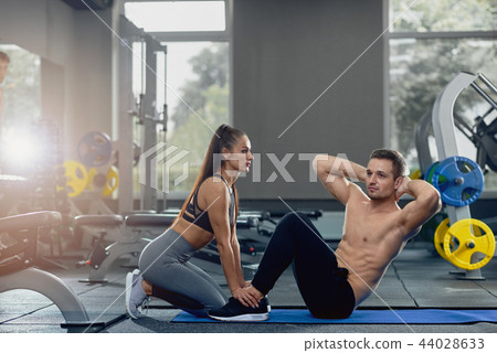 Woman holding man feet down as he doing sit up exercises. 44028633