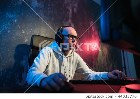 Portrait of concentrated young man in glasses and headset in dark room playing online computer game 44033776