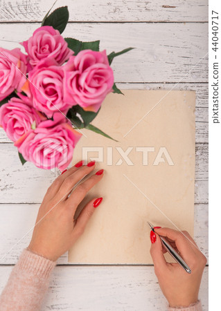 Empty blank paper with woman's hands. Background with pink roses in vase. 44040717