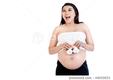 Excited pregnant woman holding pair of baby shoes over her belly 44050055