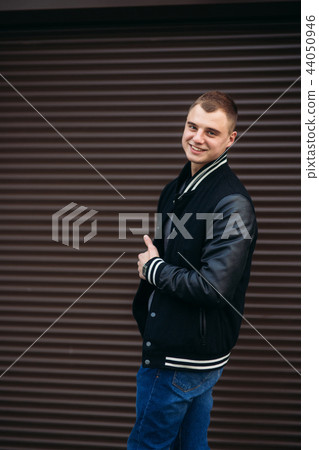 A young guy in a black jacket against a background of dark striped wall 44050946