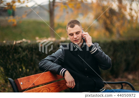 A young guy in a black jacket uses the phone 44050972