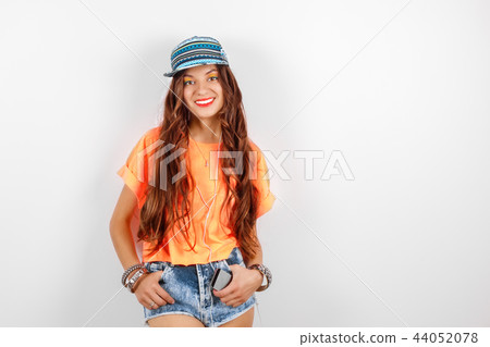 Young smiling hipster woman wearing in blue cap and orange T-shirt listening music in headphones 44052078