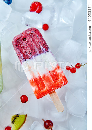 Tricolor fruit and berries ice cream on wooden stick over ice with berries, top view Tricolor fruit and berries ice cream on wooden stick over ice with berries, top view 44053374