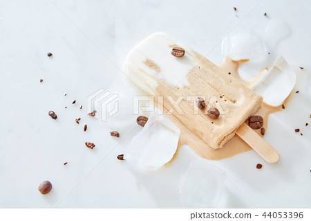 Gelato pops with milk chocolate and coffee beans on a wooden stick over stone iced table, top view Gelato pops with milk chocolate and coffee beans on a wooden stick over stone iced table, top view 44053396