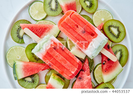 Frozen watermelon smoothies on a stick in a bowl with pieces of kiwi, lime, watermelon and slices of 44053537