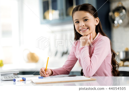 Charming positive girl writing answer in notebook Charming positive girl writing answer in notebook 44054505