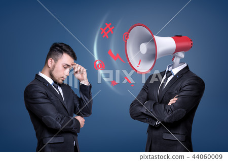 A troubled businessman stands near another man with a large shouting megaphone instead of his head. 44060009