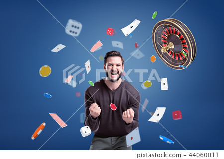 An emotional man cries angrily at camera, surrounded by a flying roulette, chips, cards and dice. 44060011
