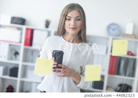 A young girl stands near a transparent board with stickers and holds a glass of coffee. 44062323