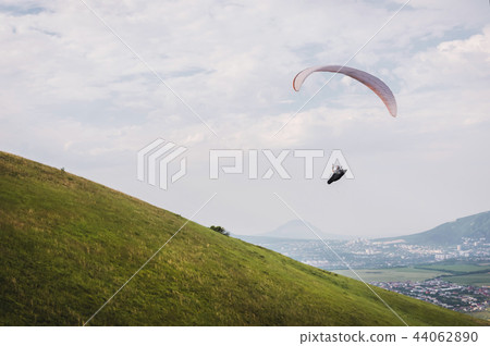 A white-orange paraglider flies over the mountainous terrain A white-orange paraglider flies over the mountainous terrain 44062890