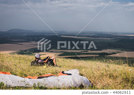 A professional paraglider in full gear and a helmet lies and rests on the grass high in the 44062911