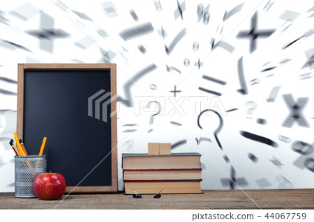 Books by slate with desk organizer and apple on wooden table 44067759