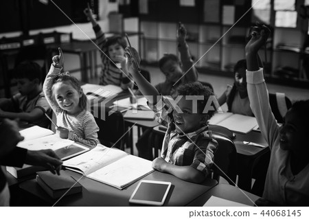 Schoolkids raising their hands in classroom 44068145