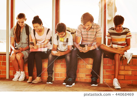 Happy students sitting on window sill and using mobile phone in corridor Happy students sitting on window sill and using mobile phone in corridor 44068469