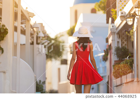 Santorini travel tourist brunette woman in red dress visiting famous white Oia village. Santorini travel tourist brunette woman in red dress visiting famous white Oia village. 44068925