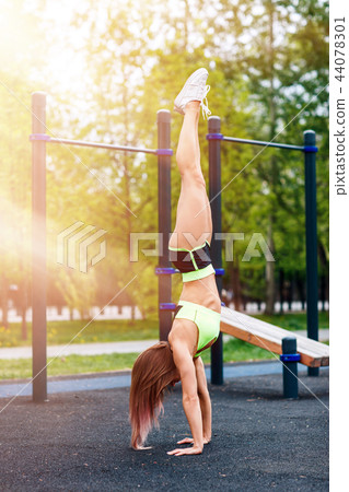 Young sporty woman stands on hand in the park. Young sporty woman stands on hand in the park. 44078301