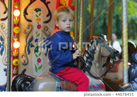 Closeup happy kid riding toy horse on the carousel. Cute baby boy in the amusement park 44078455