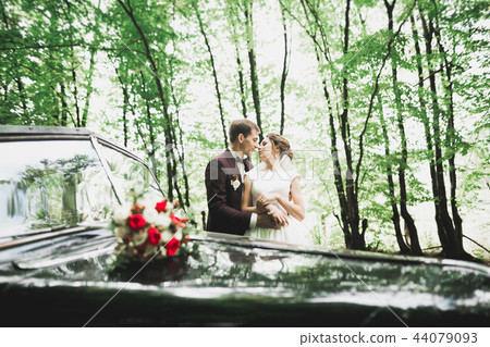 Beautiful newlywed couple posing near retro black car Beautiful newlywed couple posing near retro black car 44079093