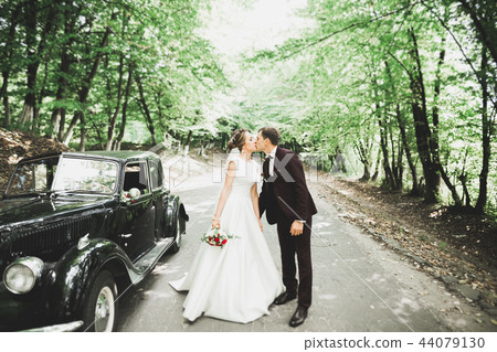 Beautiful newlywed couple posing near retro black car Beautiful newlywed couple posing near retro black car 44079130