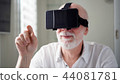 Handsome senior man in white using VR 360 glasses at home. Making browse and tap gestures 44081781