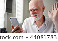 Senior man sitting at home with smartphone. Using mobile talking via messenger app. Smiling waving 44081783
