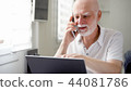 Senior man sitting at home with laptop and smartphone. Using cellphone discussing project on screen 44081786