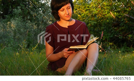 Girl student sitting on the green grass in the Park and reading a book. Girl student sitting on the green grass in the Park and reading a book. 44085765