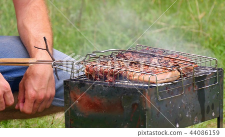 A man prepares large pieces of meat on the grill, turning for roasting. Relax and cook on an open A man prepares large pieces of meat on the grill, turning for roasting. Relax and cook on an open 44086159