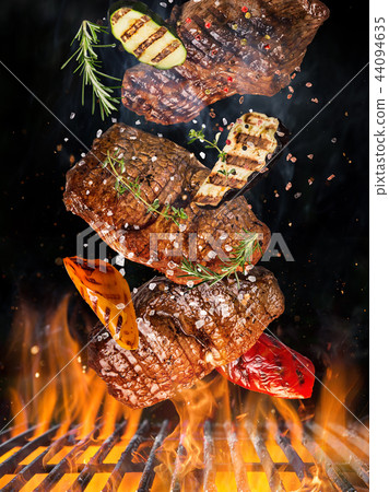Tasty beef steaks flying above cast iron grate with fire flames. 44094635