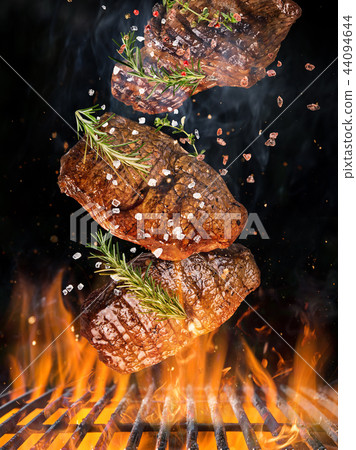 Tasty beef steaks flying above cast iron grate with fire flames. Tasty beef steaks flying above cast iron grate with fire flames. 44094644
