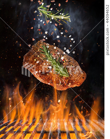 Tasty beef steak flying above cast iron grate with fire flames. 44094652