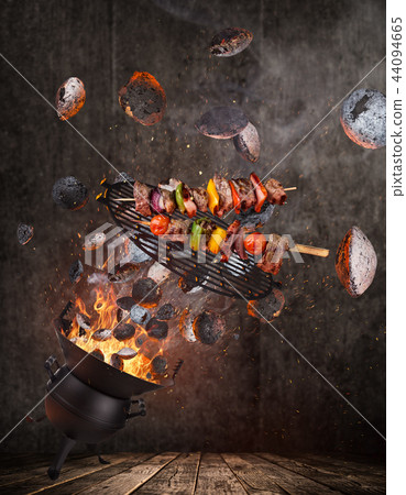 Kettle grill with hot briquettes, cast iron grate and tasty skewers flying in the air. Kettle grill with hot briquettes, cast iron grate and tasty skewers flying in the air. 44094665