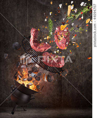 Kettle grill with hot briquettes, cast iron grate and tasty meats flying in the air. 44094707