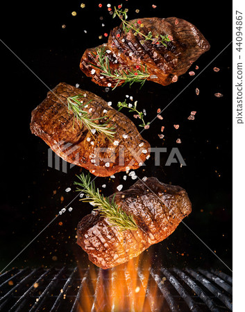 Tasty beef steaks flying above cast iron grate with fire flames. Tasty beef steaks flying above cast iron grate with fire flames. 44094867