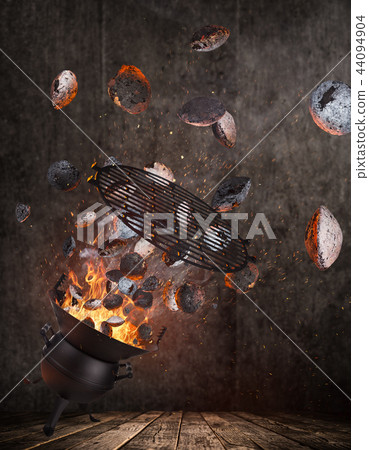 Kettle grill with hot briquettes and cost iron grid flying in the air. 44094904
