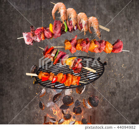 Kettle grill with hot briquettes, cast iron grate and tasty skewers flying in the air. 44094982