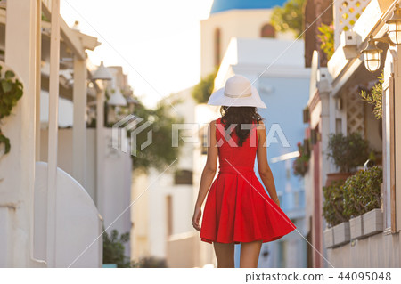 Santorini travel tourist brunette woman in red dress visiting famous white Oia village. 44095048