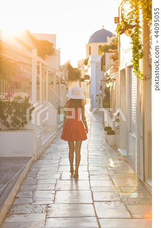 Santorini travel tourist brunette woman in red dress visiting famous white Oia village. Santorini travel tourist brunette woman in red dress visiting famous white Oia village. 44095055