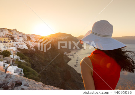 Santorini travel tourist brunette woman in red dress visiting famous white Oia village. Santorini travel tourist brunette woman in red dress visiting famous white Oia village. 44095056