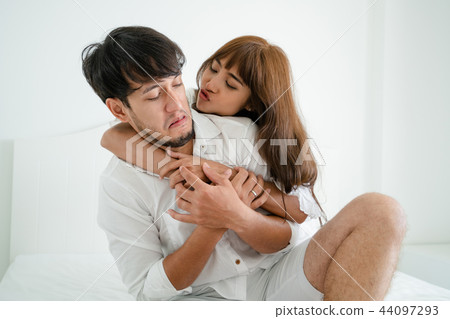 Playful young couple teasing in home bedroom. 44097293