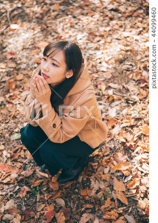 Woman sitting on a carpet of fallen leaves Woman sitting on a carpet of fallen leaves 44099460