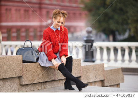 Pretty smiling curly redhaired girl with black leather backpack is sitting on the street, autumn Pretty smiling curly redhaired girl with black leather backpack is sitting on the street, autumn 44109037