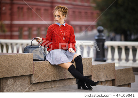 Pretty smiling curly redhaired girl with black leather backpack is sitting on the street, autumn Pretty smiling curly redhaired girl with black leather backpack is sitting on the street, autumn 44109041