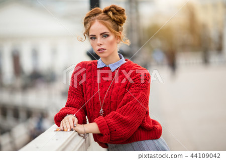 Pretty smiling curly redhaired girl is wearing red knitted sweater walking on the street, autumn Pretty smiling curly redhaired girl is wearing red knitted sweater walking on the street, autumn 44109042