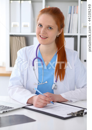 Ginger female doctor filling up medical form on clipboard closeup. Healthcare, insurance and Ginger female doctor filling up medical form on clipboard closeup. Healthcare, insurance and 44109249