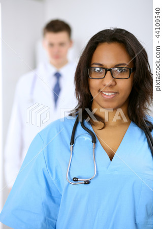 Female african american medical doctor with colleagues in background at hospital. Medicine and Female african american medical doctor with colleagues in background at hospital. Medicine and 44109540